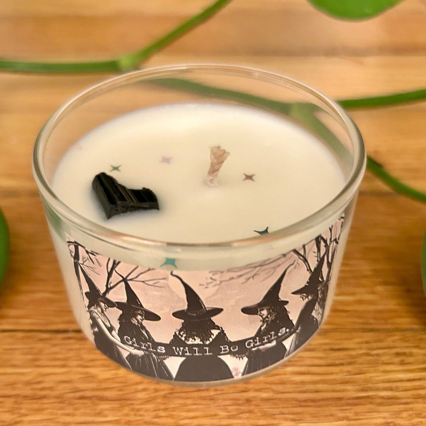 Candle in a glass jar with witch design and text on a wooden surface