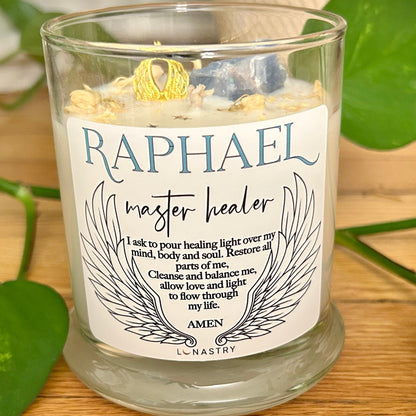 Candle labeled 'Raphael master healer' with angel wings design on a wooden surface with green leaves.