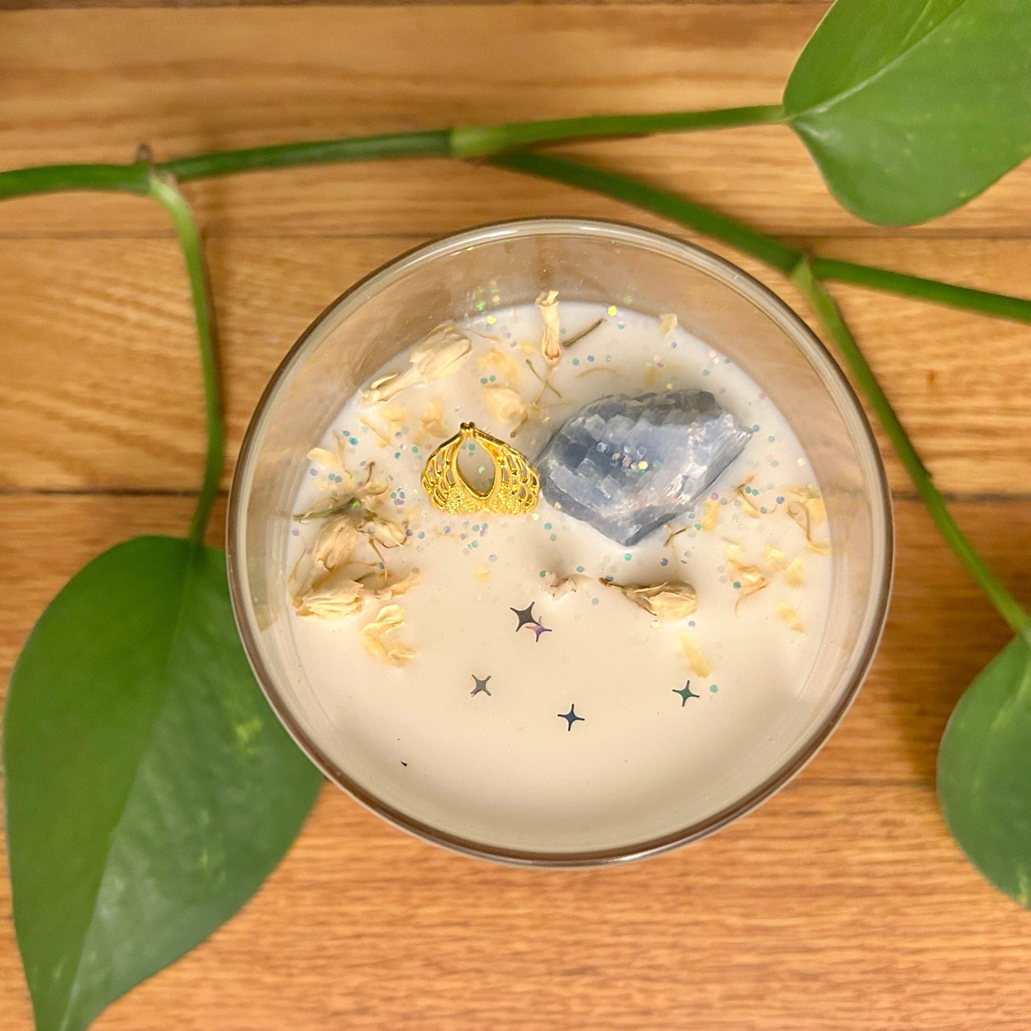 Candle in a glass container with decorative elements on a wooden surface with green leaves.
