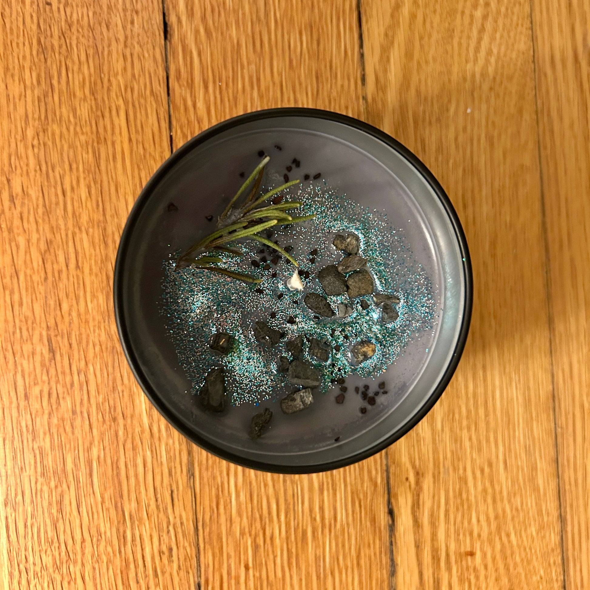 candle in black tin with with decorative stones and greenery on a wooden surface