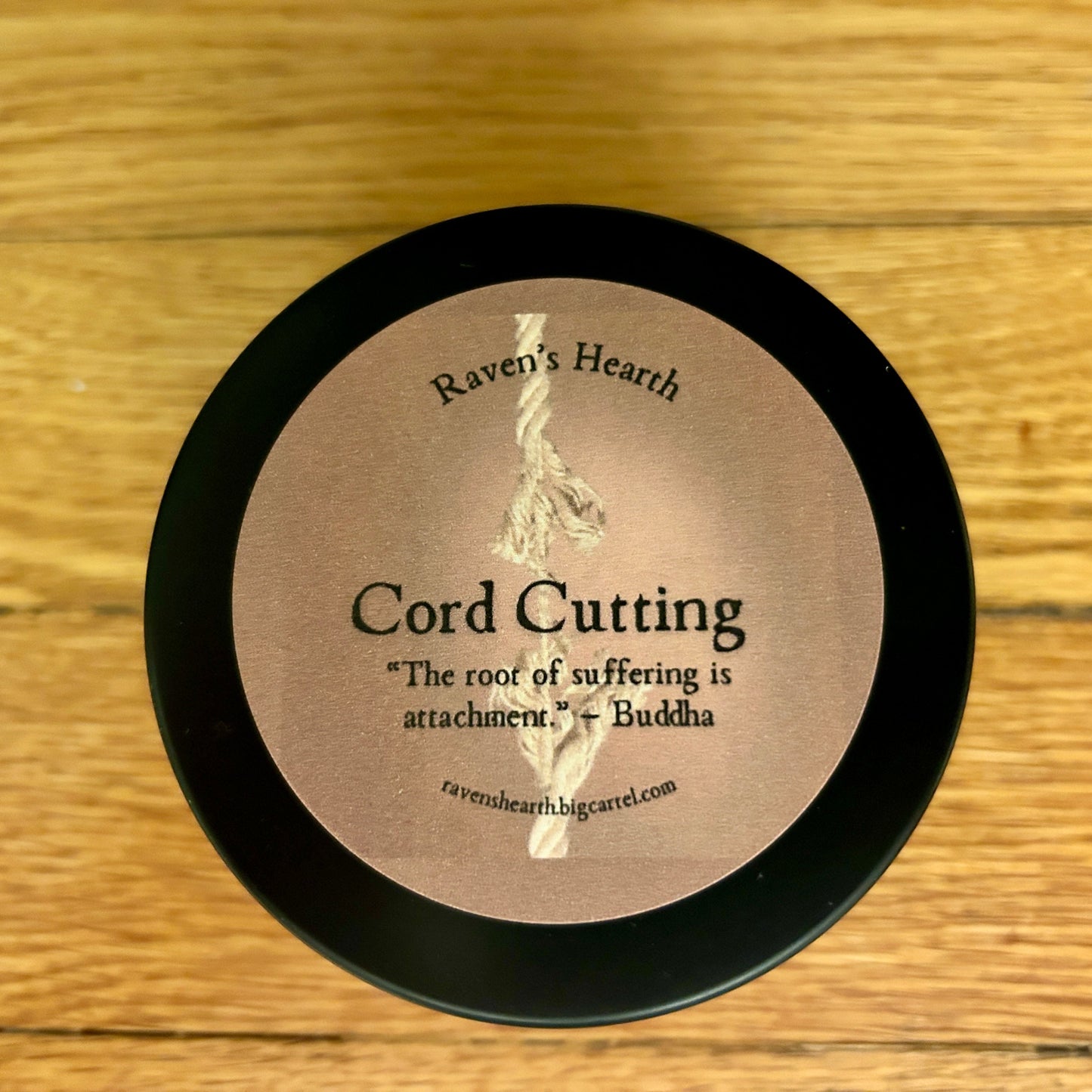 Candle container with 'Raven's Hearth' branding and cord cutting text on a wooden surface