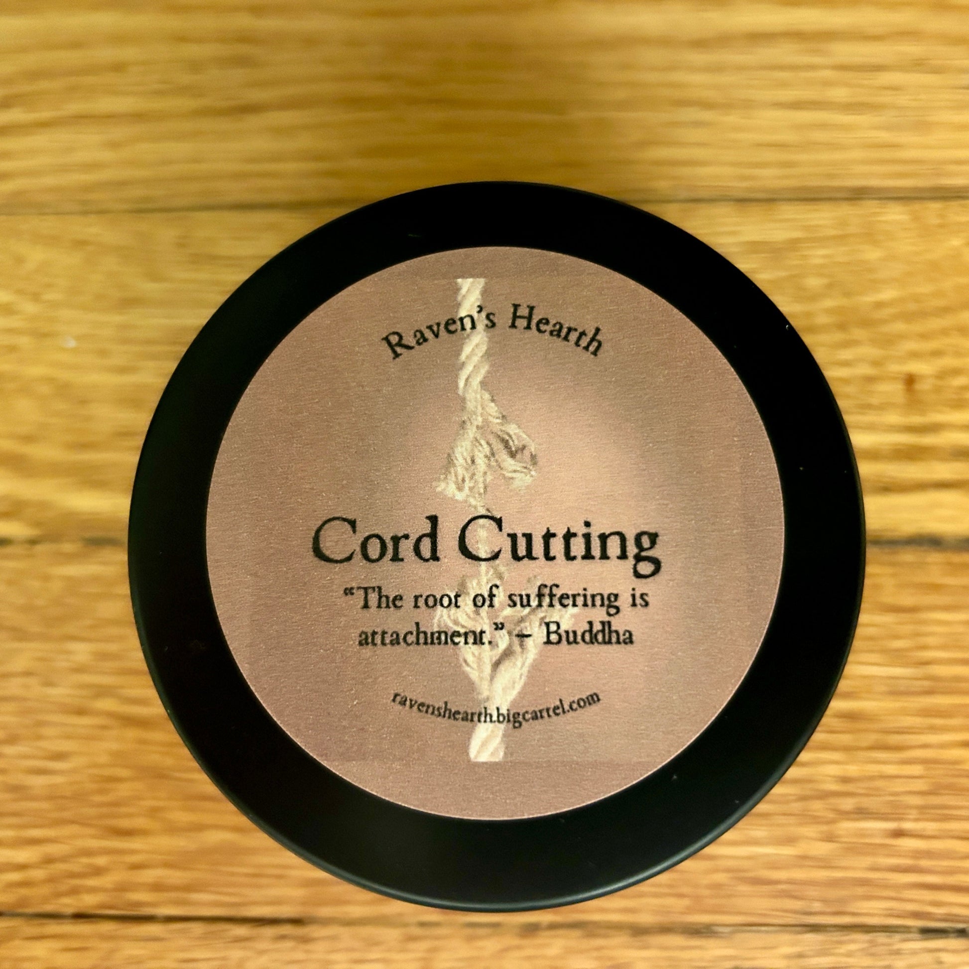 Candle container with 'Raven's Hearth' branding and cord cutting text on a wooden surface