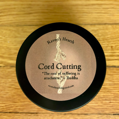 Candle container with 'Raven's Hearth' branding and cord cutting text on a wooden surface