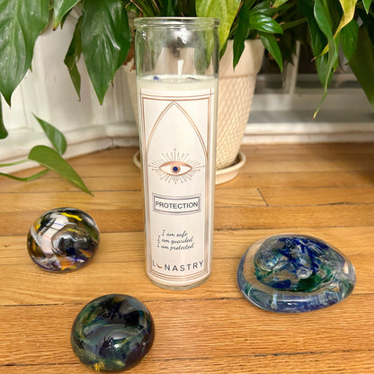 Candle labeled 'Protection' with decorative stones and plants on a wooden surface