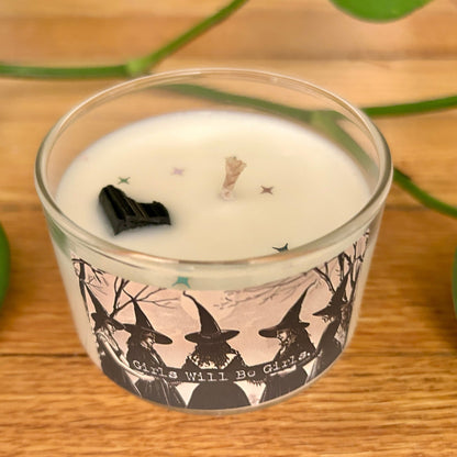 Candle in a glass jar with witch design and text on a wooden surface